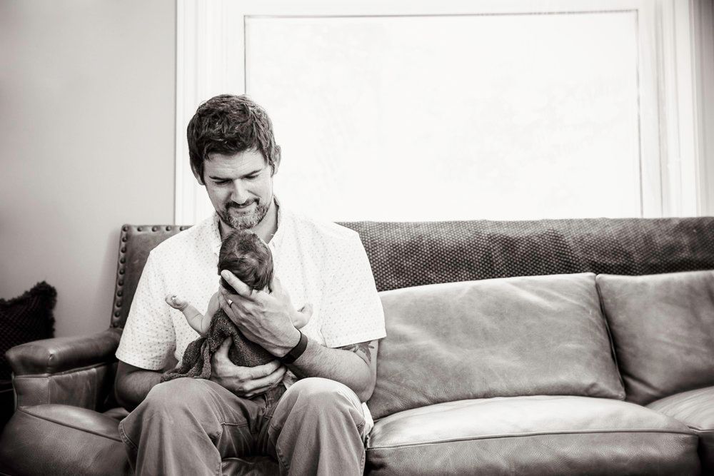 Person in white shirt sitting on couch holding and looking at newborn baby.