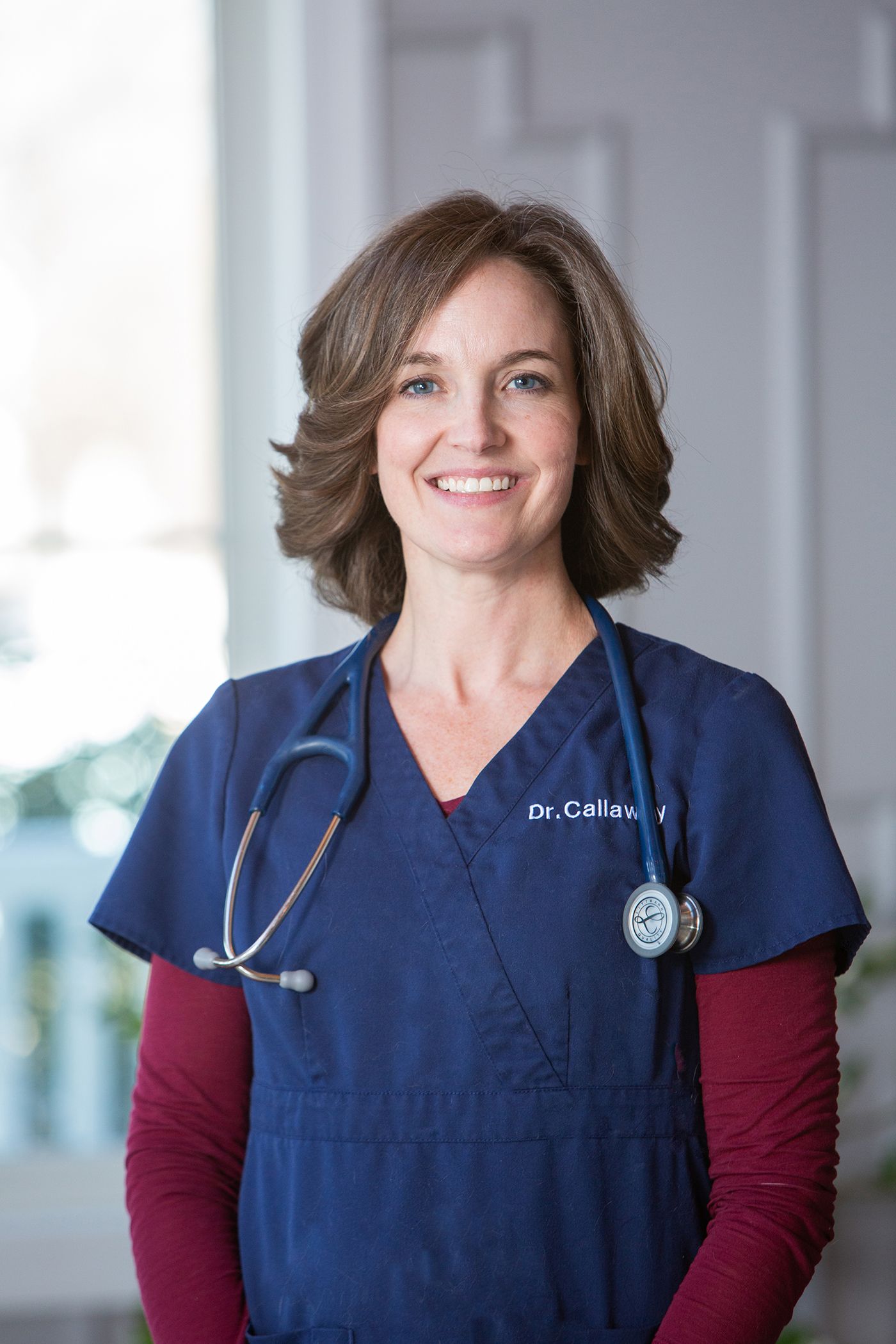 Healthcare professional wearing navy scrubs and stethoscope in medical setting.