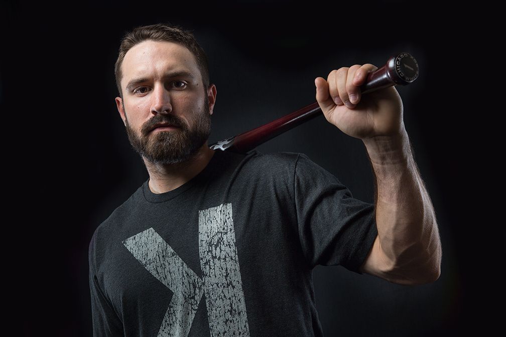 Dark dramatic portrait of baseball player holding bat against black background.