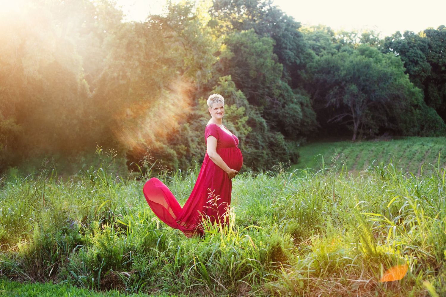 A flowing red dress moves gracefully in a sunlit meadow during golden hour as sunbeams illuminate the natural landscape.