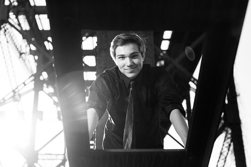 Black and white photo of a smiling young man framed by metal structure with dramatic light rays.