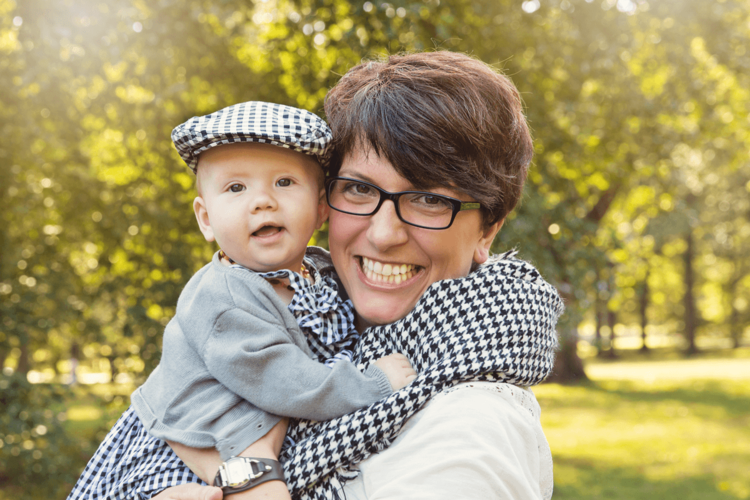 A joyful parent and baby wearing matching checkered patterns pose together outside.