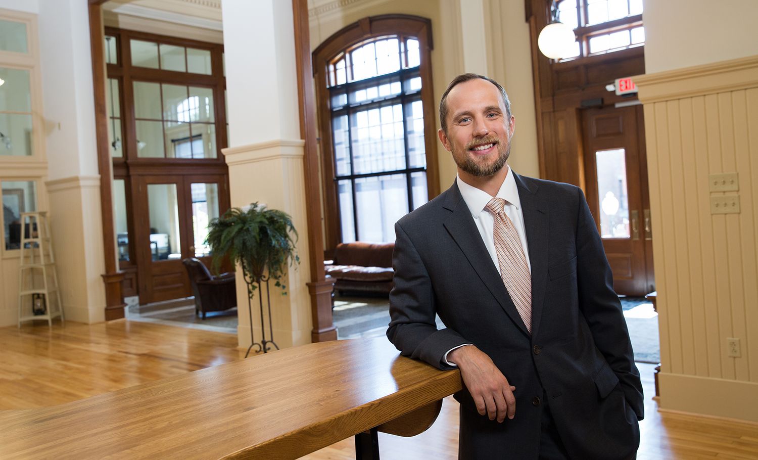 Professional in a dark suit smiles confidently while standing in an elegant historic building interior.
