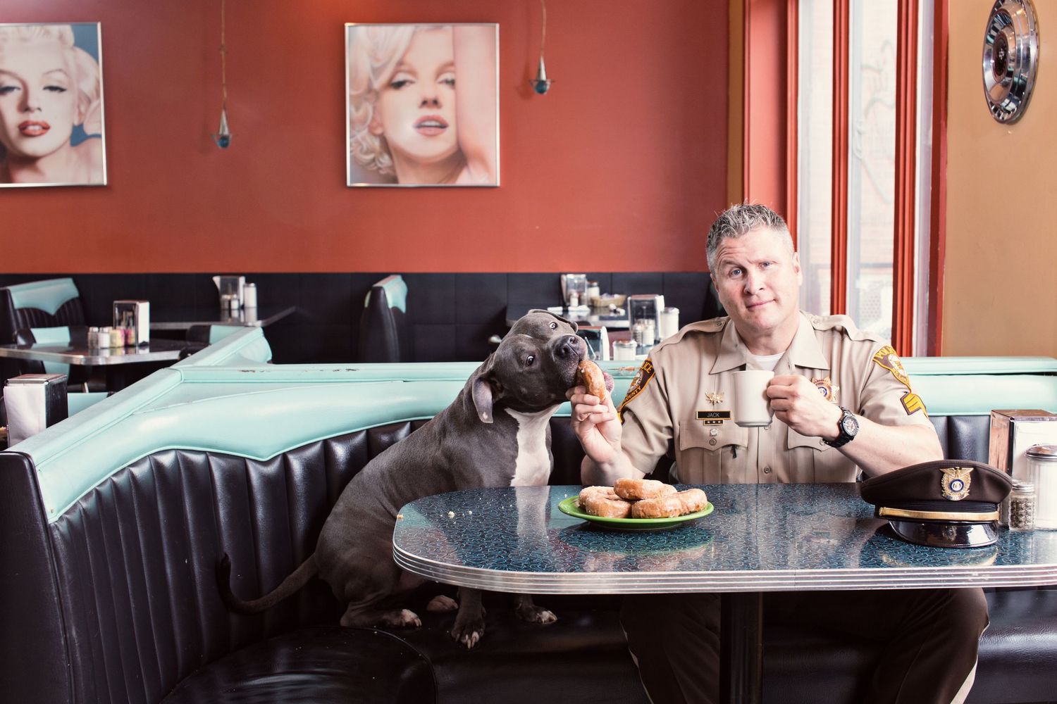 A dog and diner share a meal at a retro-style booth in a restaurant.