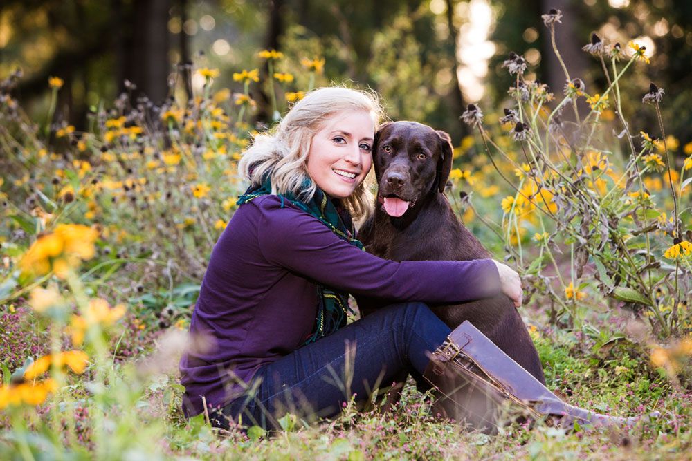 A chocolate Labrador and companion share a tender moment among yellow wildflowers.