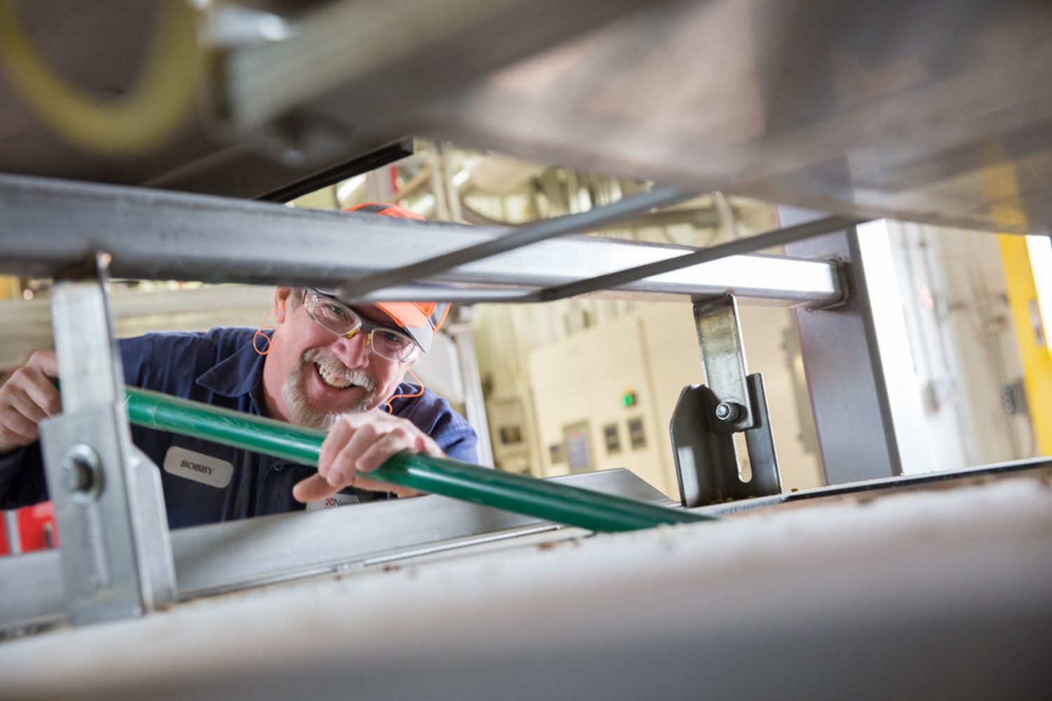 Industrial worker performing maintenance check through equipment access panel.