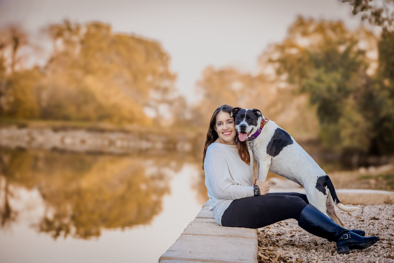 A beautiful autumn scene with a person and an Australian Shepherd dog sitting by a reflective pond.