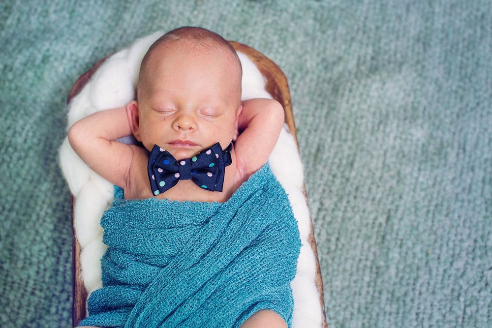 Peaceful sleeping newborn wrapped in soft turquoise blanket on grey background.