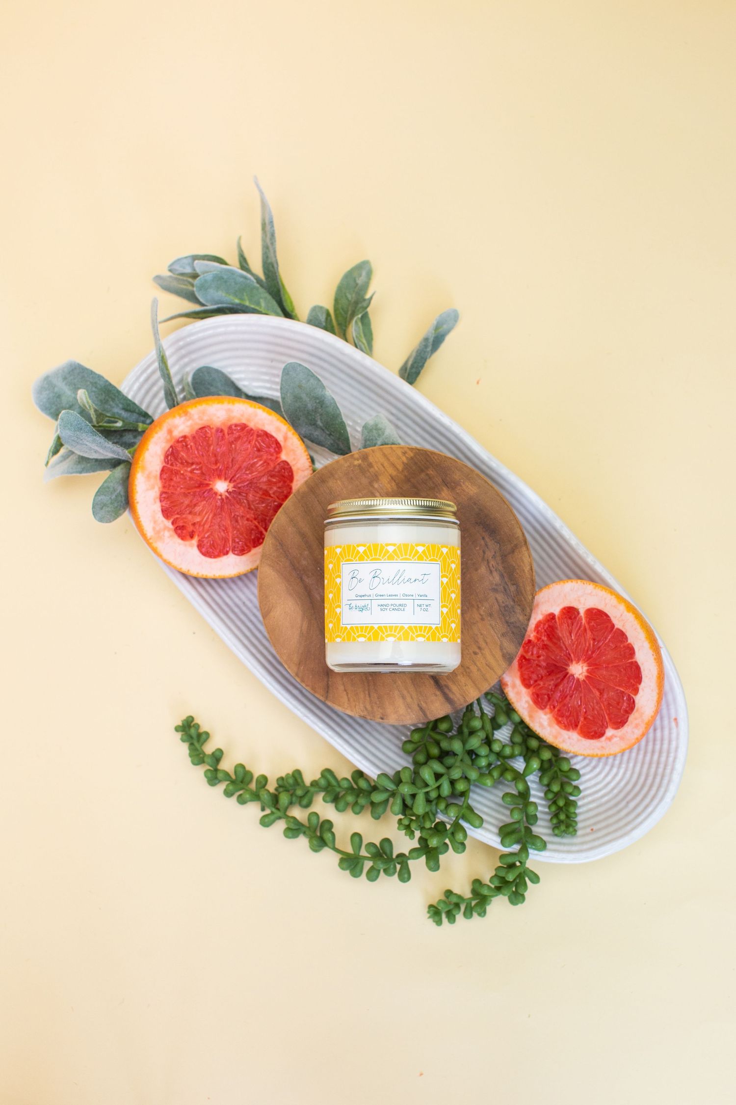 Citrus-themed candle jar displayed with grapefruit halves and greenery on oval platter.