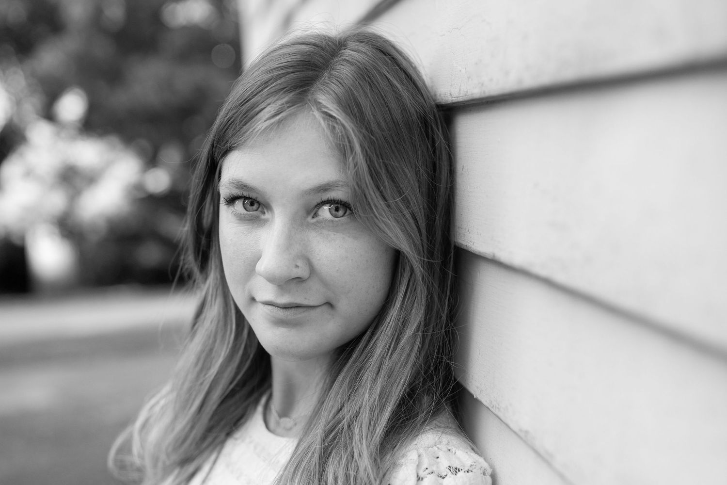 Black and white portrait of a young woman with long hair leaning against a wall outdoors.