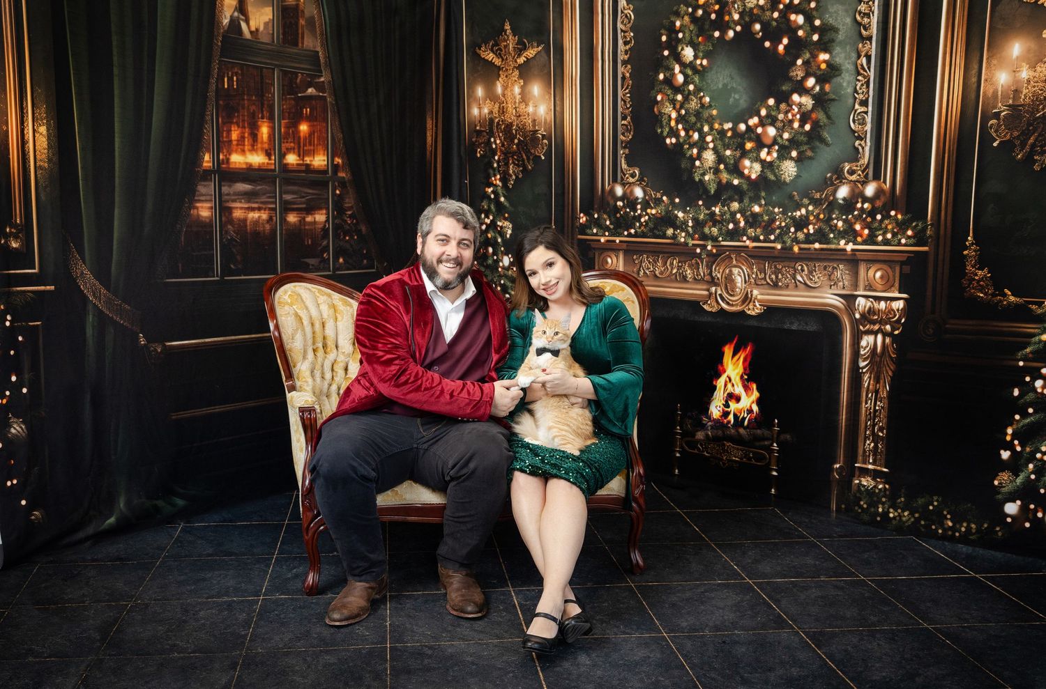 Couple in red and green outfits sitting on a vintage sofa by a fireplace with Christmas decorations.
