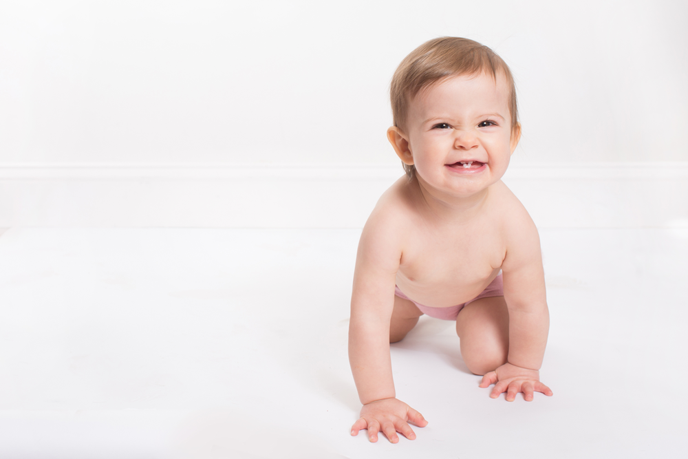 Baby in diaper crawling on white background with happy expression.