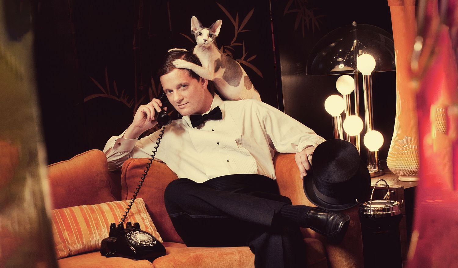 Retro-styled scene with Chihuahua perched on couch while using vintage telephone.