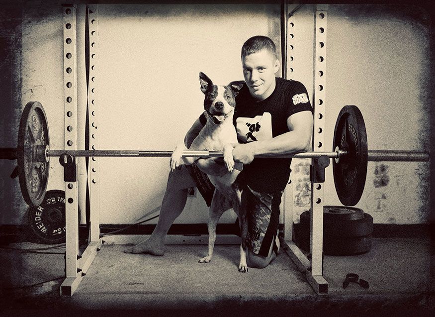 A vintage-style gym photo shows a dog watching its companion prepare to lift weights.