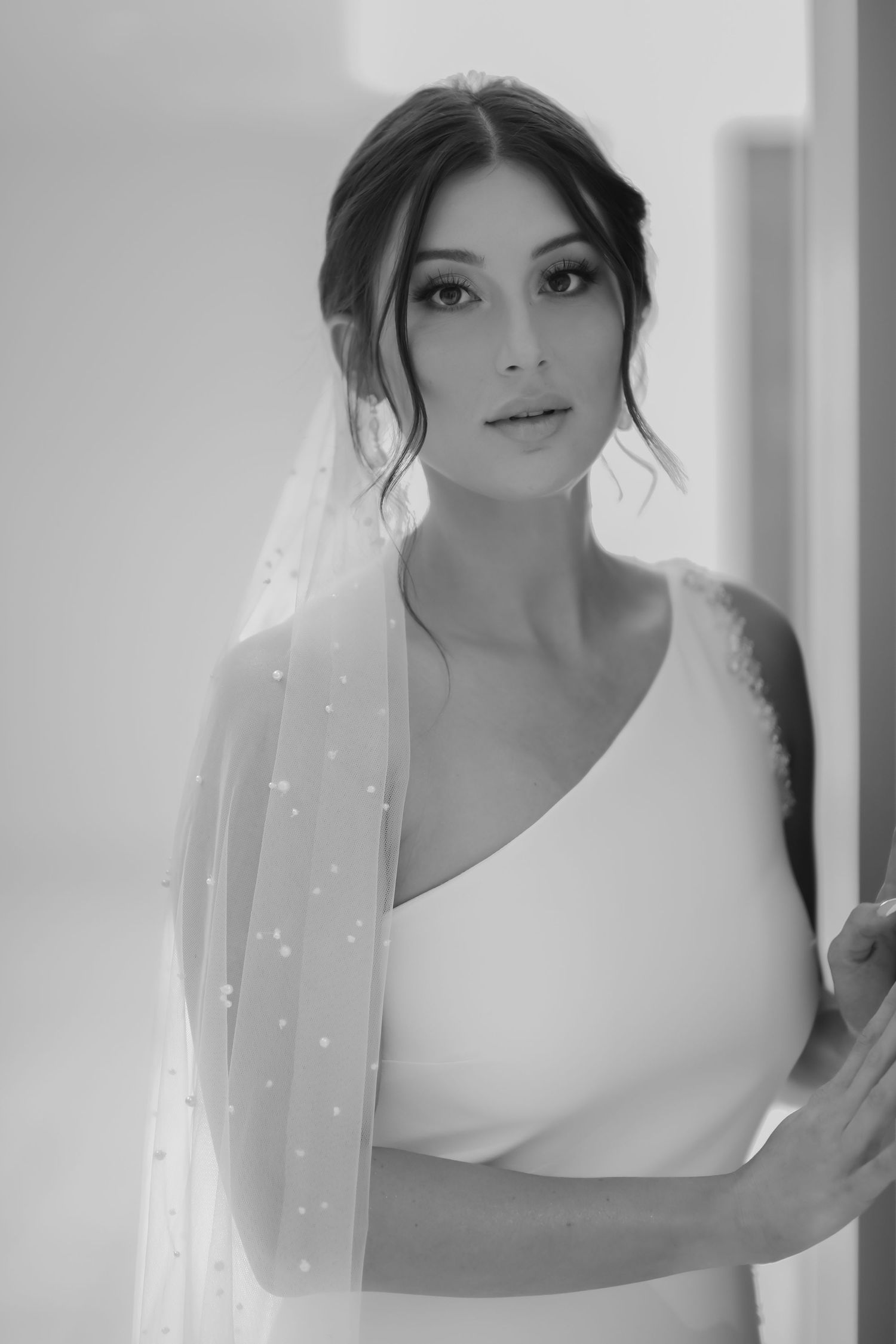 Elegant black and white bridal portrait with soft lighting, romantic veil and one shoulder wedding dress.