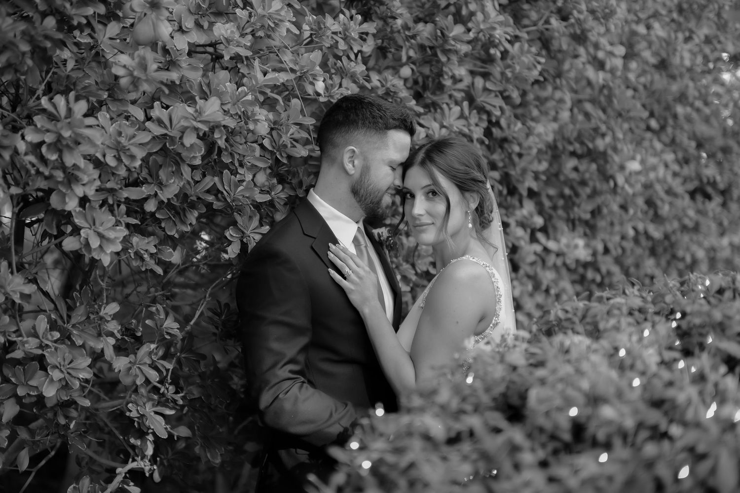 An intimate black and white wedding portrait among lush garden foliage.