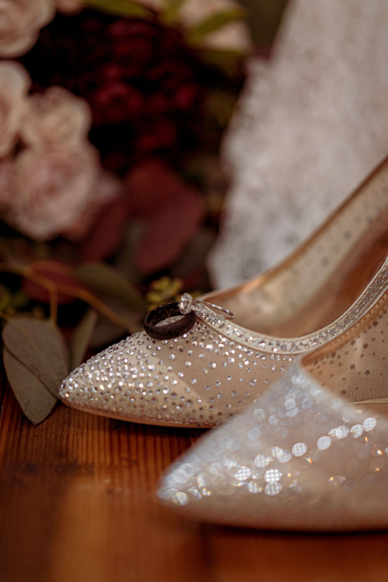 Sparkling rhinestone bridal shoe with wedding rings placed on wooden surface.
