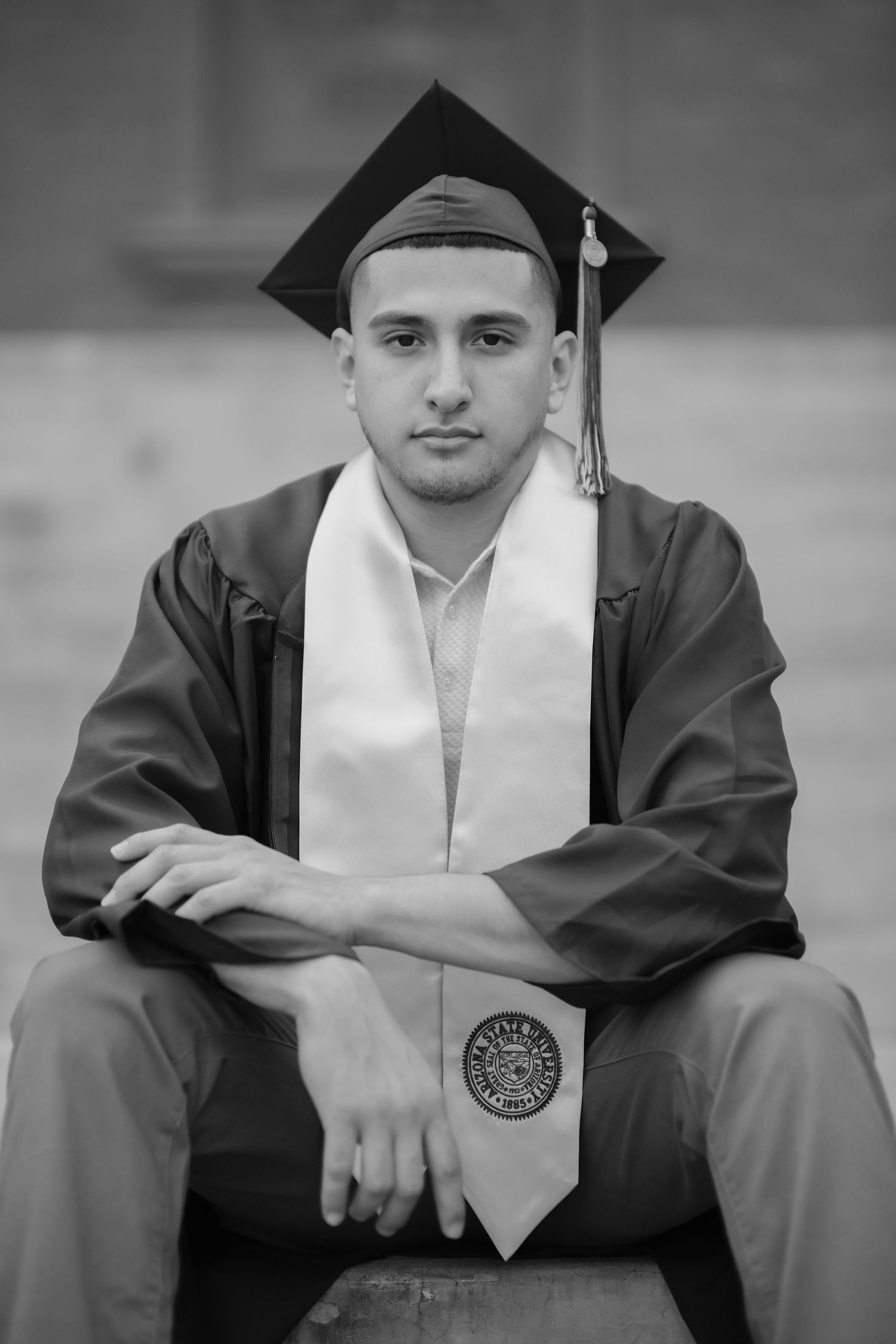 Graduate in traditional cap and gown poses formally for black and white graduation photo.