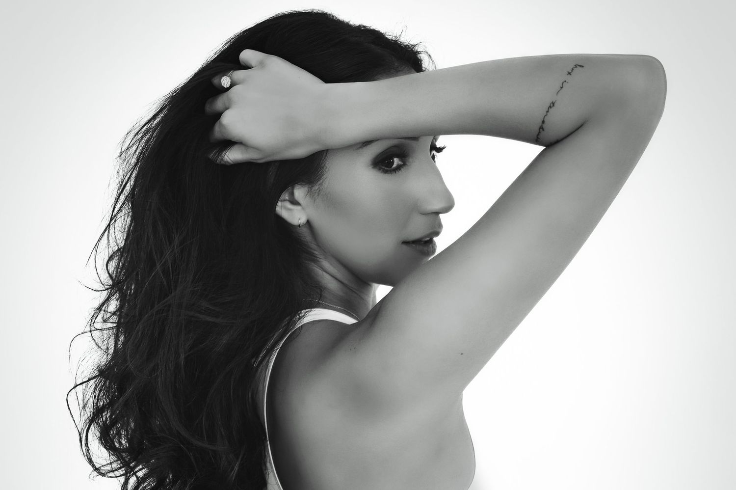 Black and white portrait of a woman with long dark hair posing with her arm raised against a light background.