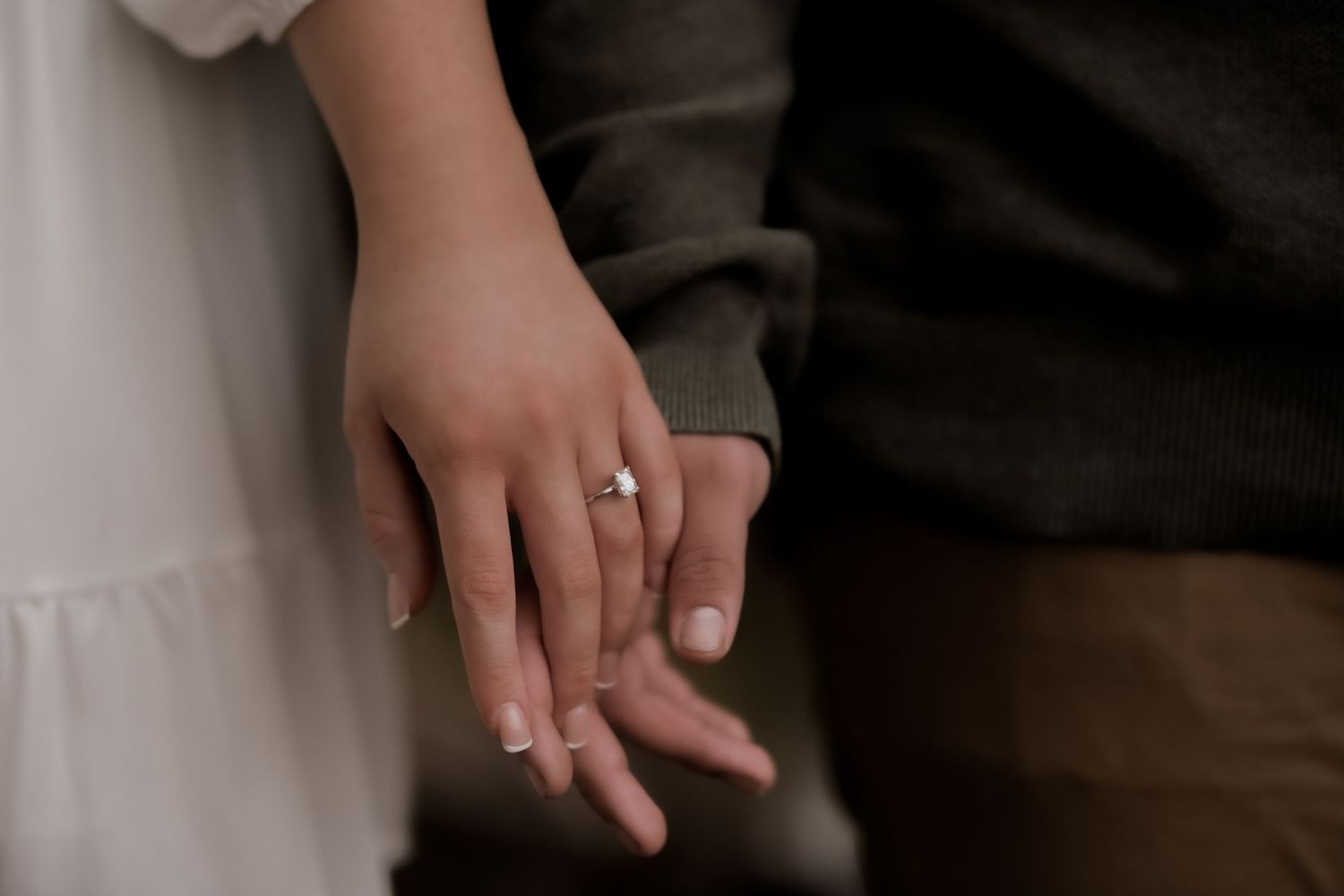 Close-up shot of hands with engagement ring in gentle embrace.
