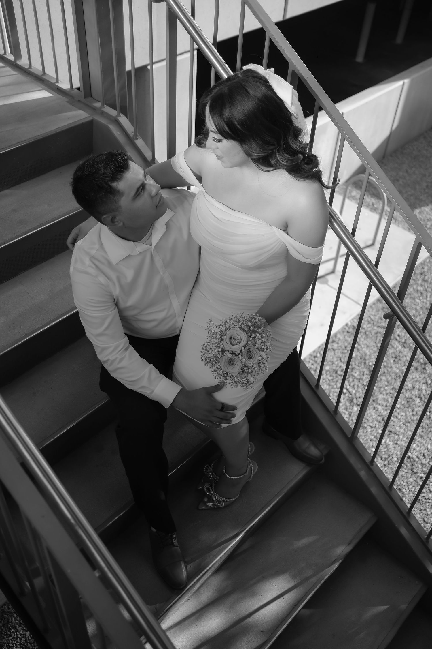 A couple in formal attire shares a romantic moment on a staircase in black and white photography.