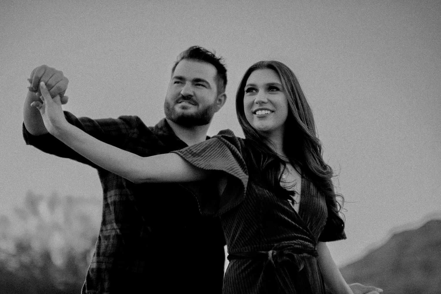 Black and white photo of dancing couple against mountain landscape.