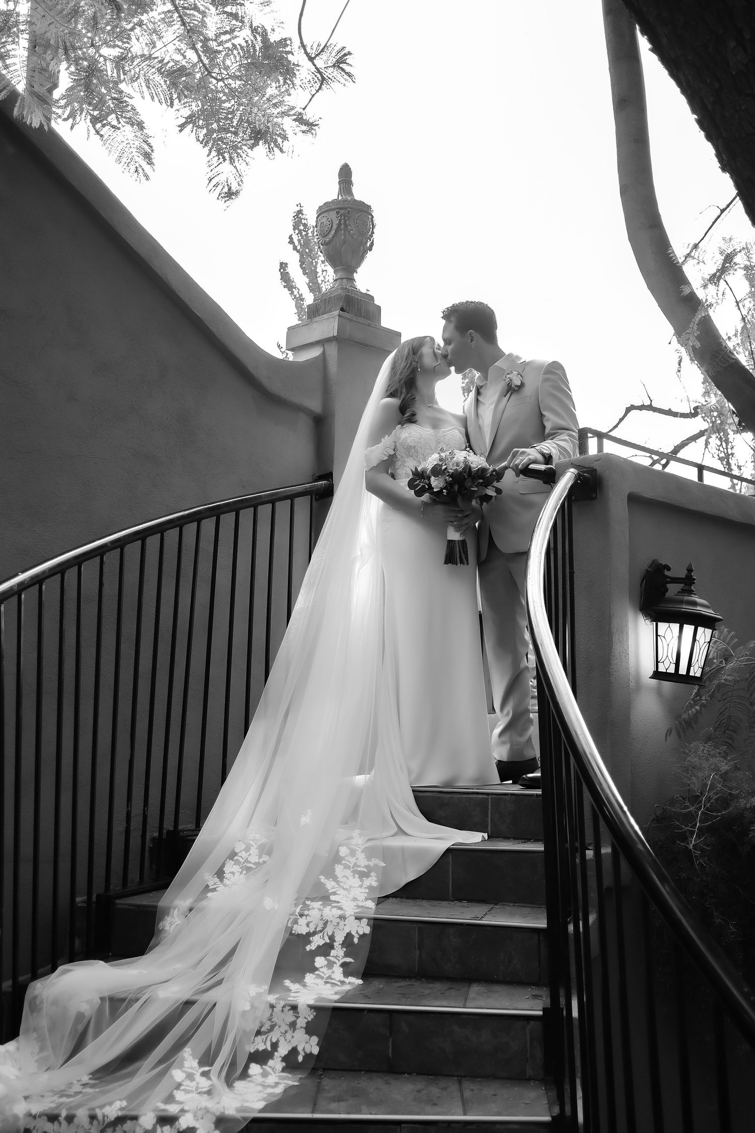 A series of black and white wedding photos showing a bride ascending stairs in a flowing white gown with a long train.