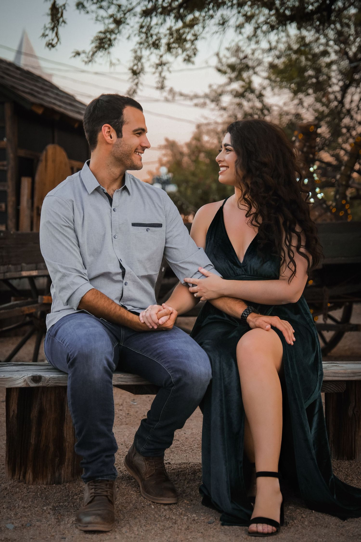 A couple shares a joyful moment while sitting on a wooden bench at sunset.