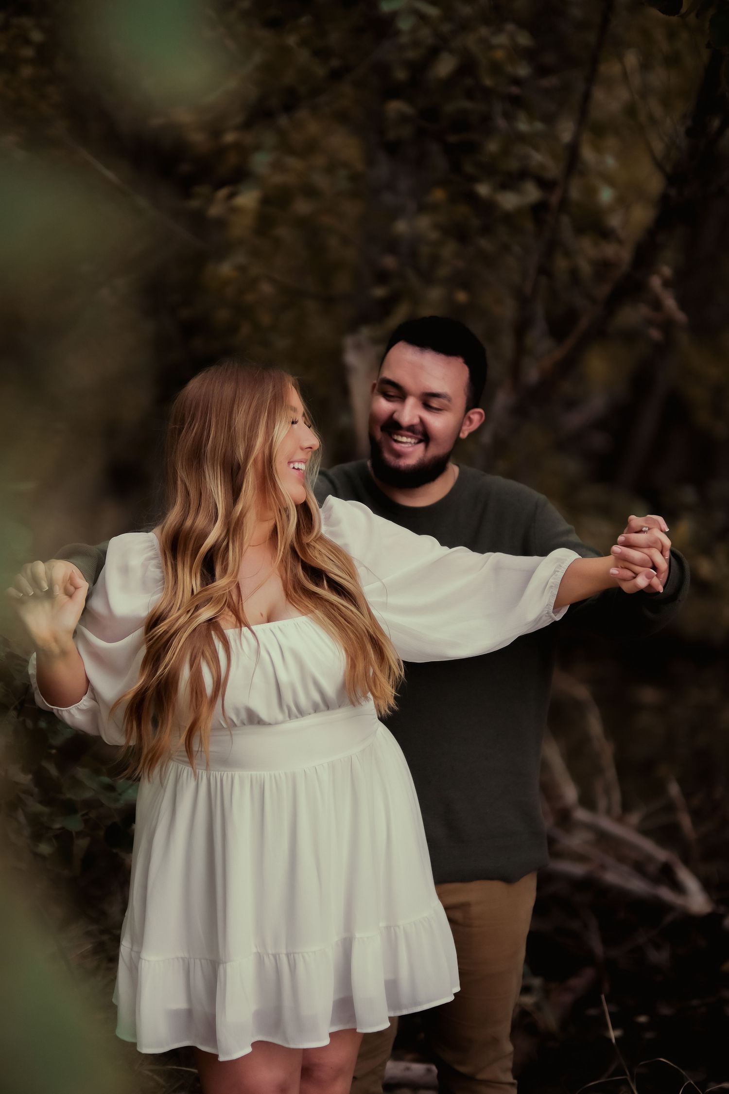 A couple dances joyfully together in a forest setting with natural lighting.