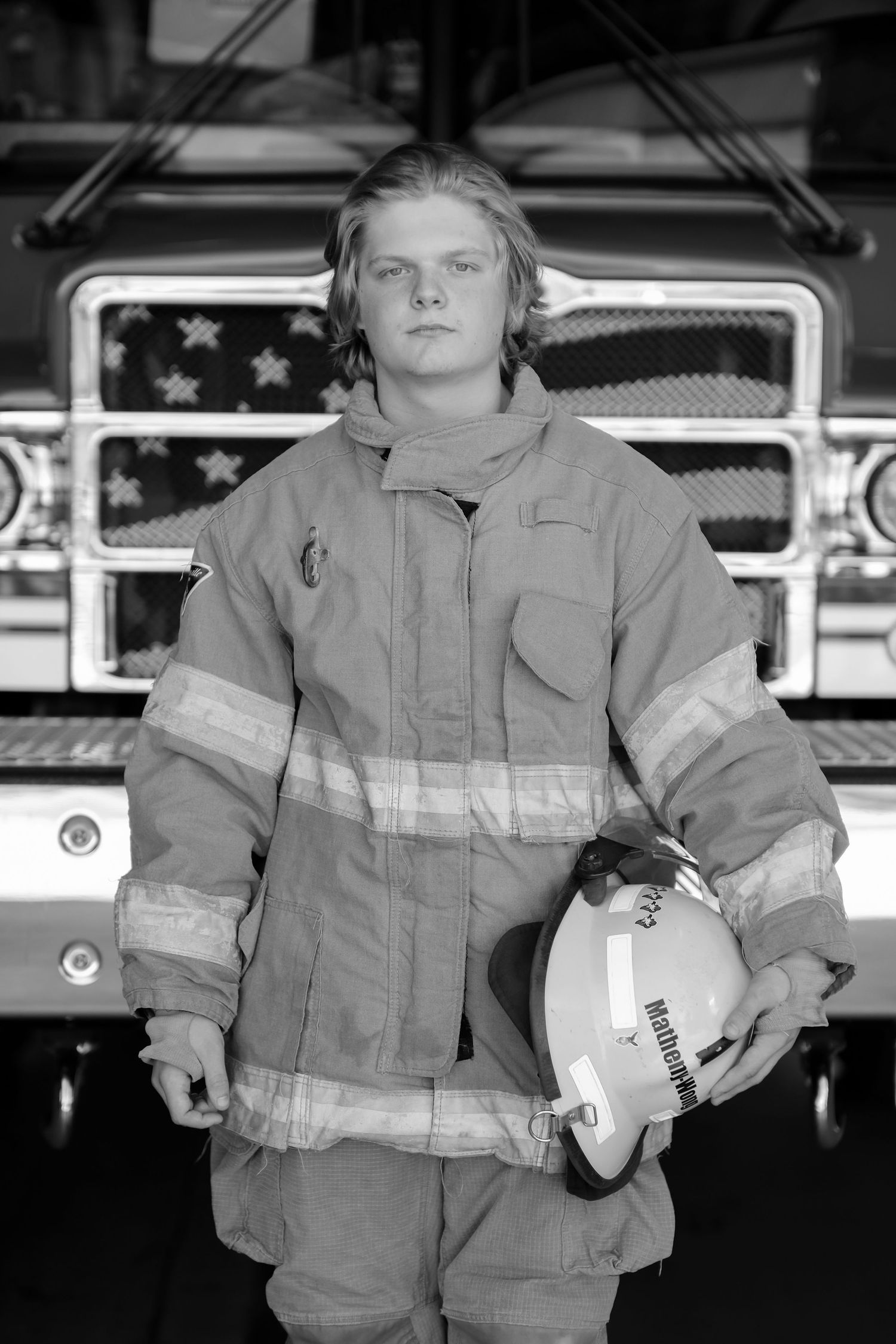 Firefighter in full protective gear poses in front of fire truck with helmet.
