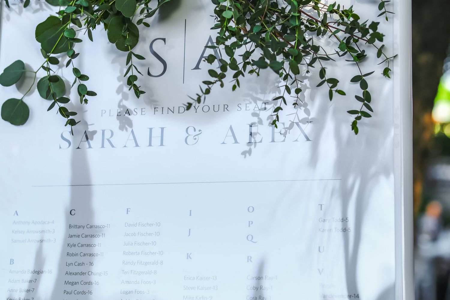 Elegant wedding seating chart sign for Sarah & Alex, decorated with greenery garlands at an outdoor reception.