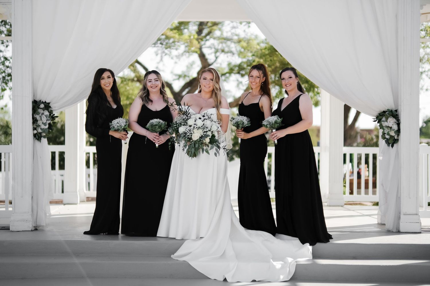 Wedding party in black and white attire posed under white gazebo.