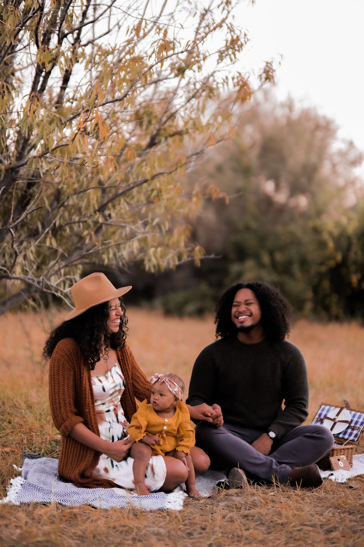 Family enjoying picnic on blanket under autumn trees in golden light.