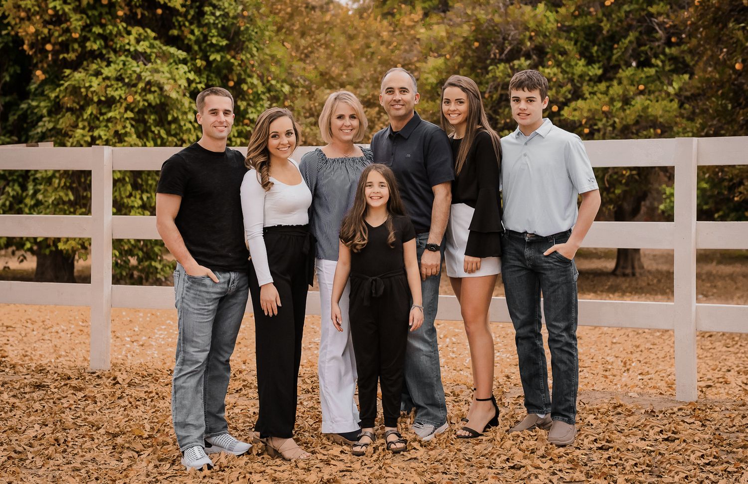A group posed together outdoors on an autumn day wearing casual attire against wooden fencing.