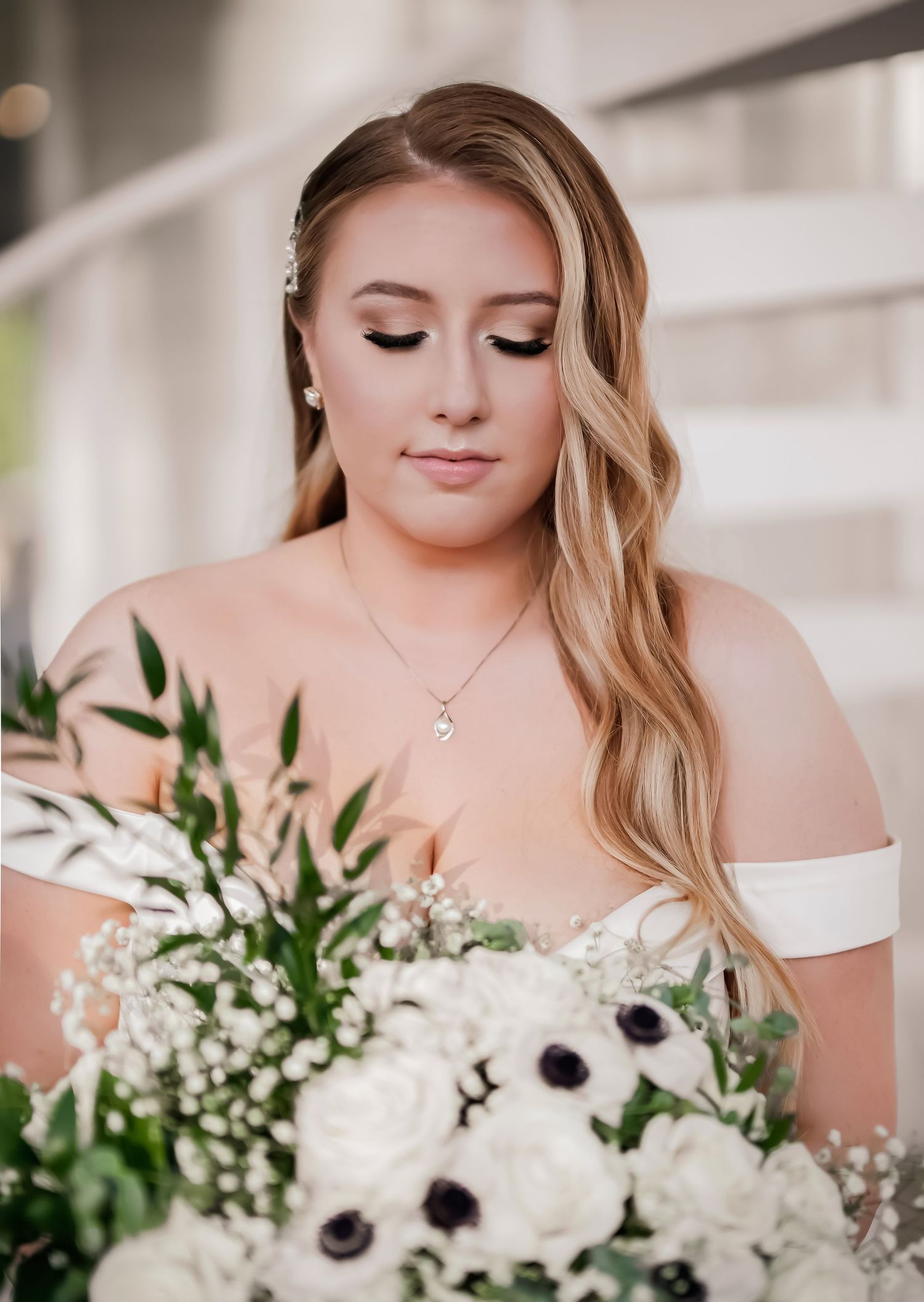 A bride in an off-shoulder dress holds a romantic white and anemone flower bouquet with greenery.