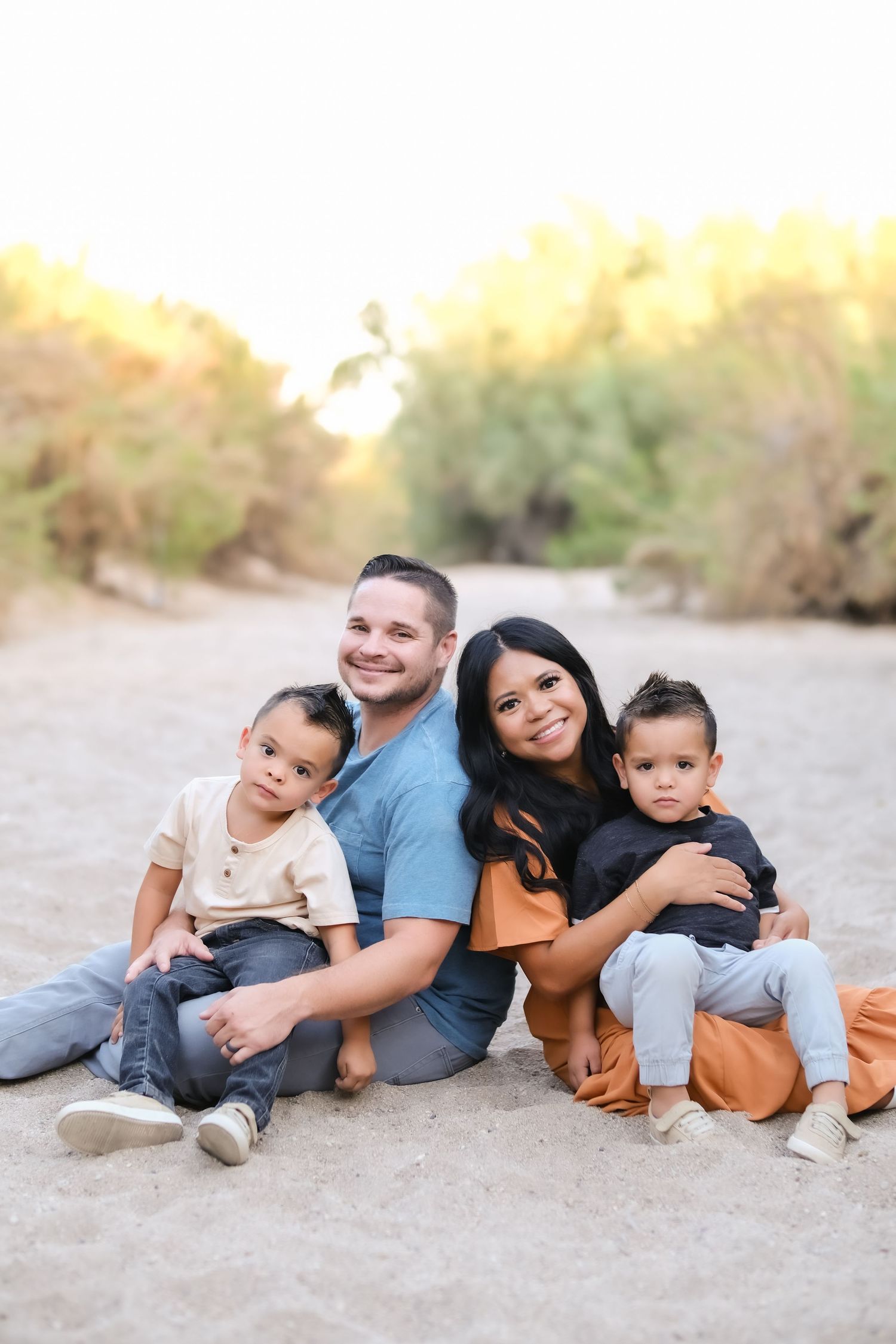Family of four sits together on sandy ground during golden hour photoshoot.