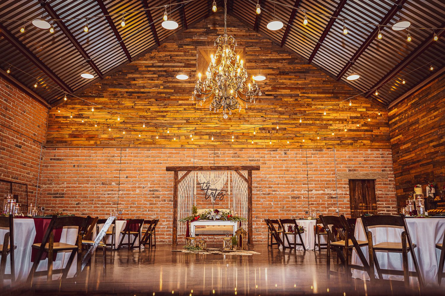Rustic barn wedding venue with wooden walls, chandelier, and ceremony arch setup.