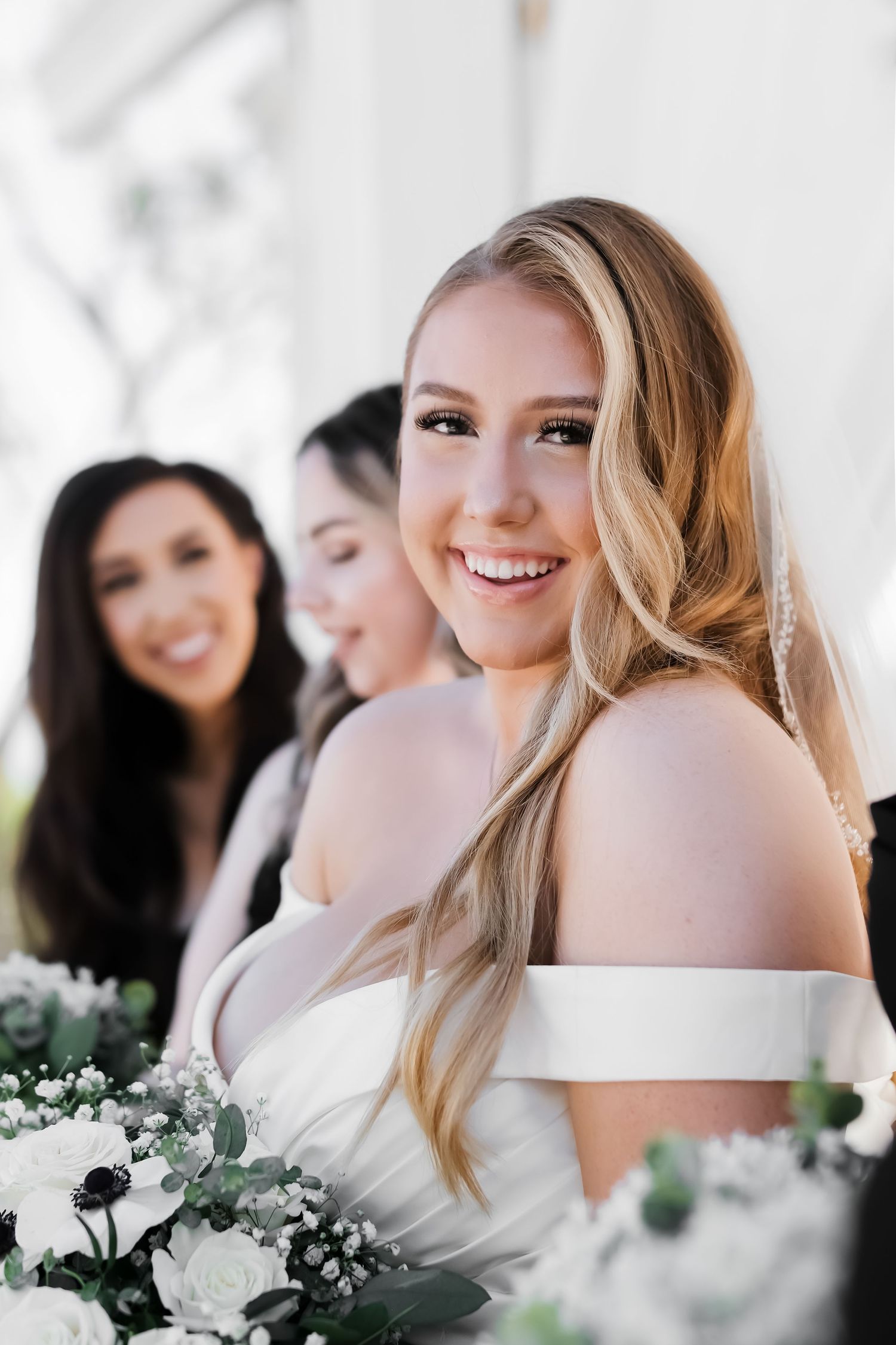 Joyful bride with bridesmaids sharing candid moment with white floral bouquets.