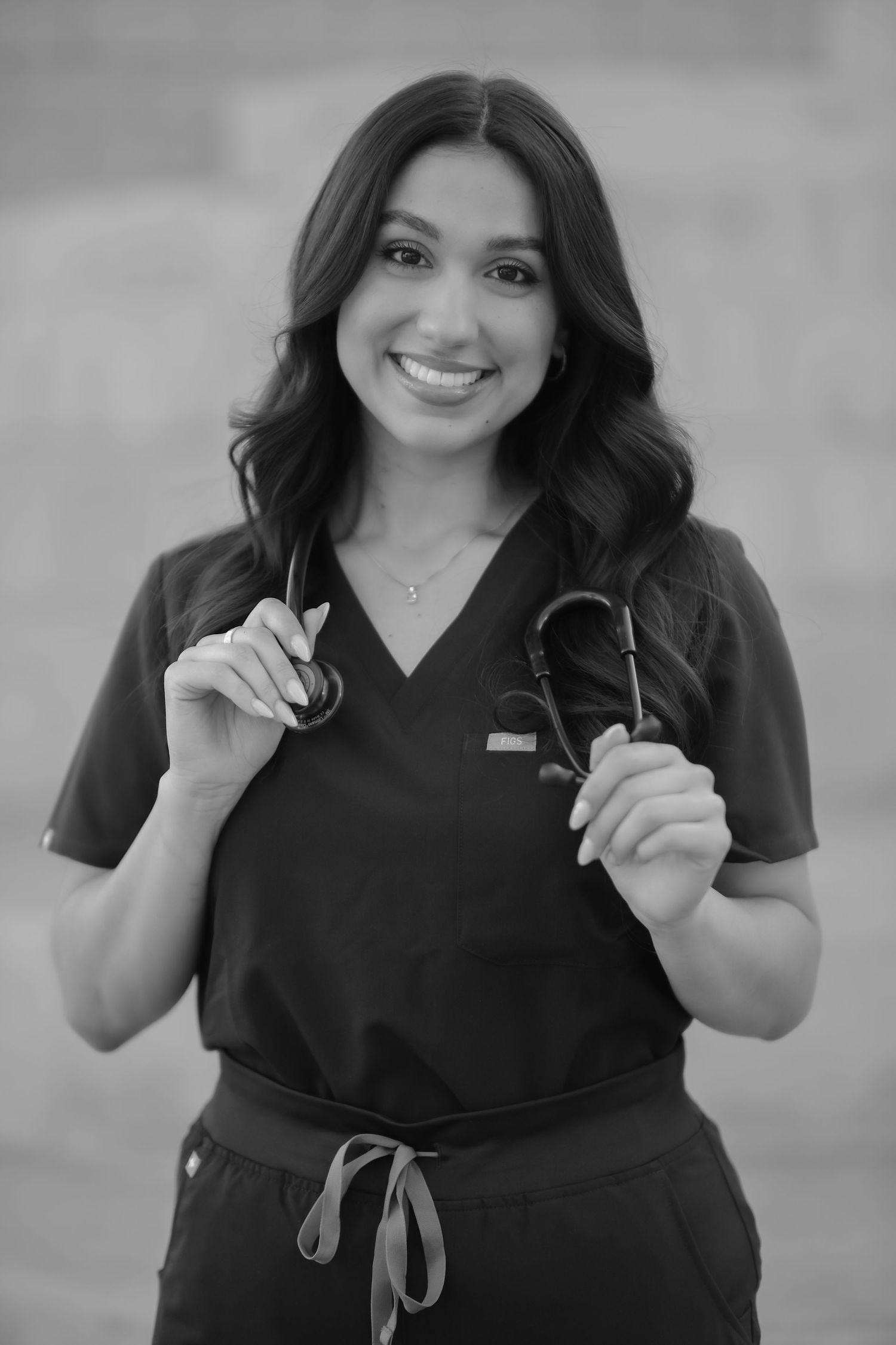 Healthcare professional in dark scrubs holds medical equipment while smiling at camera.