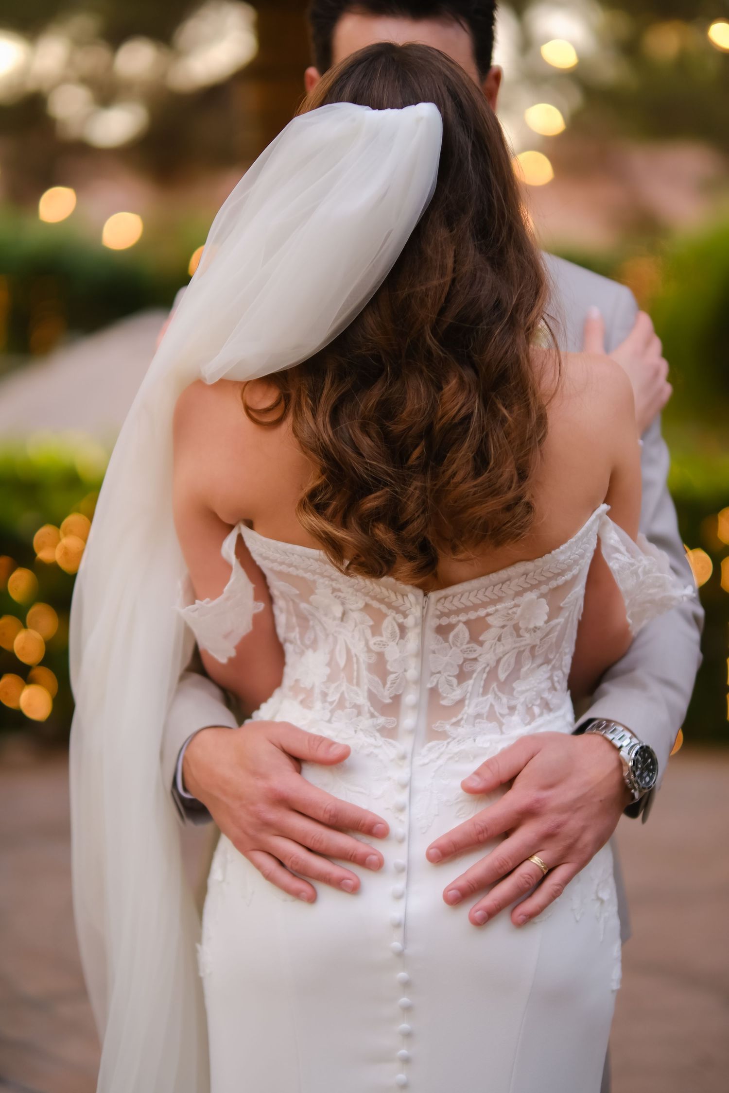 Close-up of detailed lace wedding dress back with hands embracing.