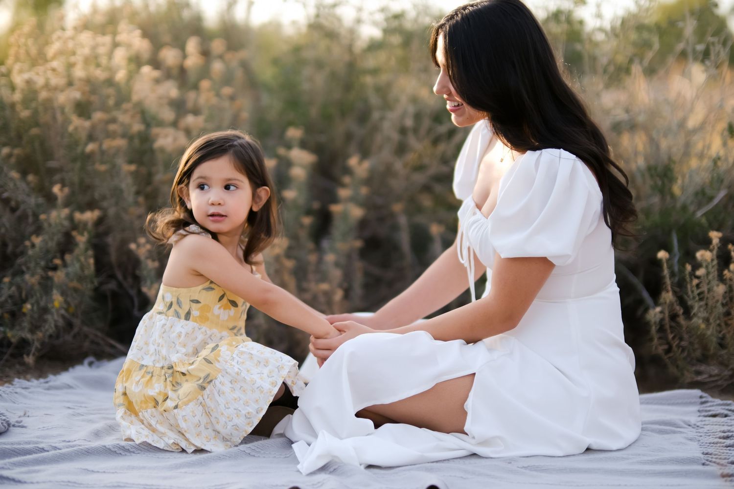 Mother and daughter share tender moment while sitting on blanket outdoors.