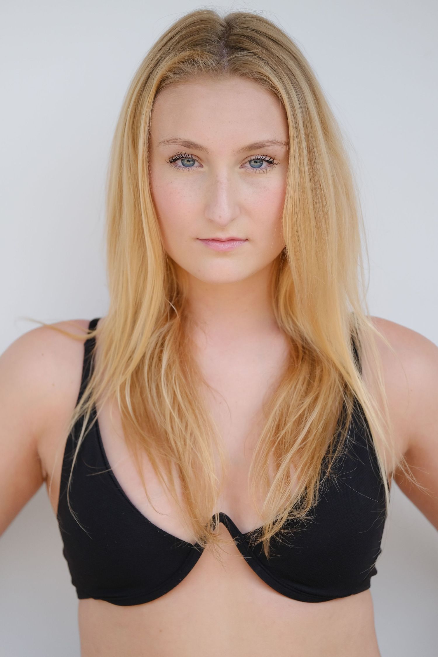 Close-up portrait against white background showing long blonde hair and black top.