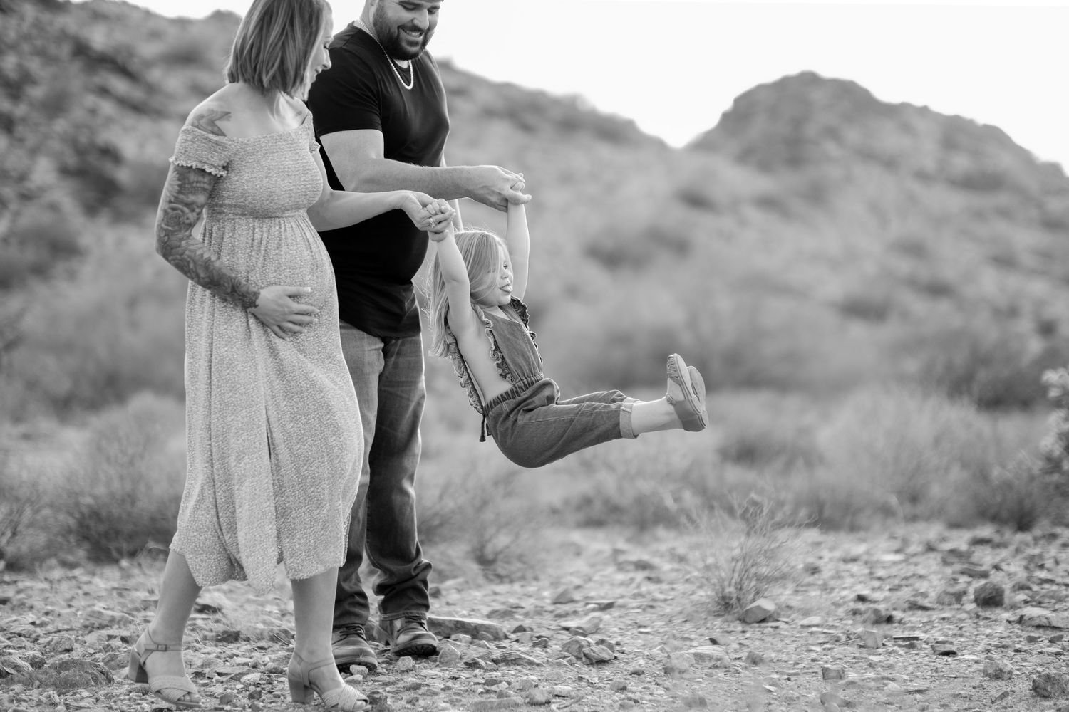 A couple share a playful moment against a desert mountain backdrop in black and white.