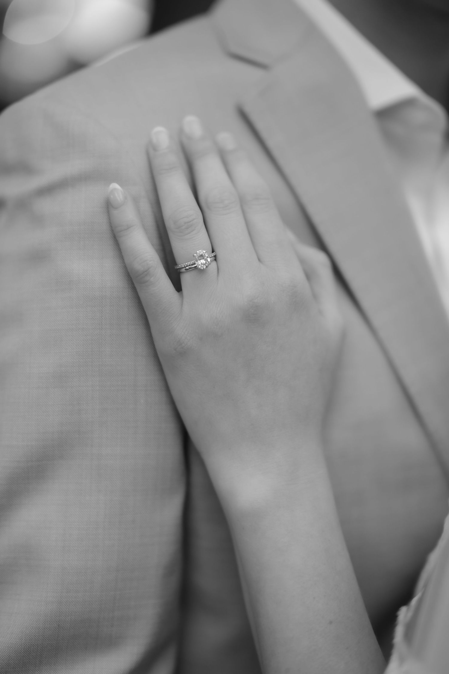 A delicate hand rests gently showing off an elegant engagement ring in a black and white photograph.