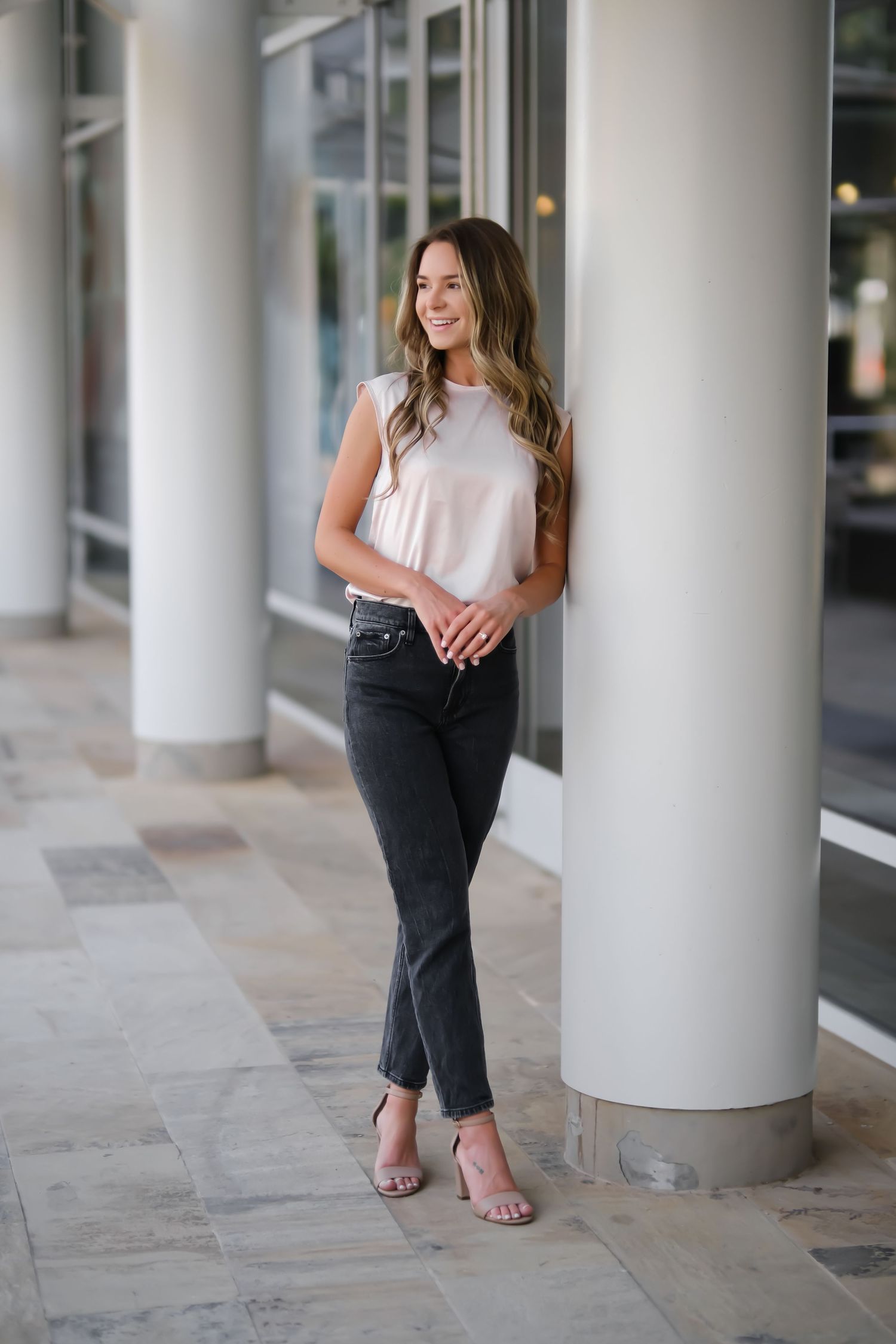 Woman in casual attire poses between columns at modern shopping center.