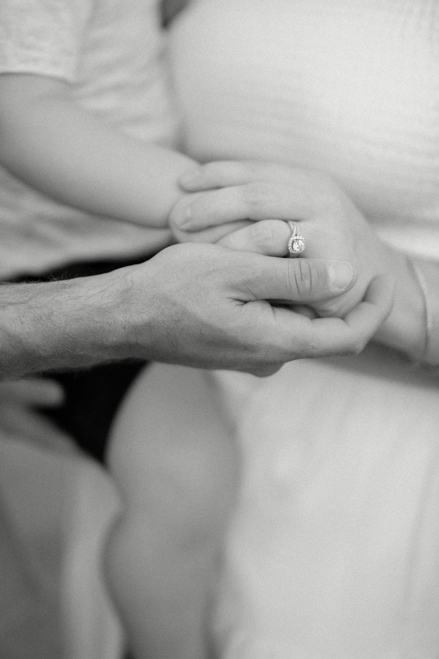 Close up black and white photo of hands holding with engagement ring visible.