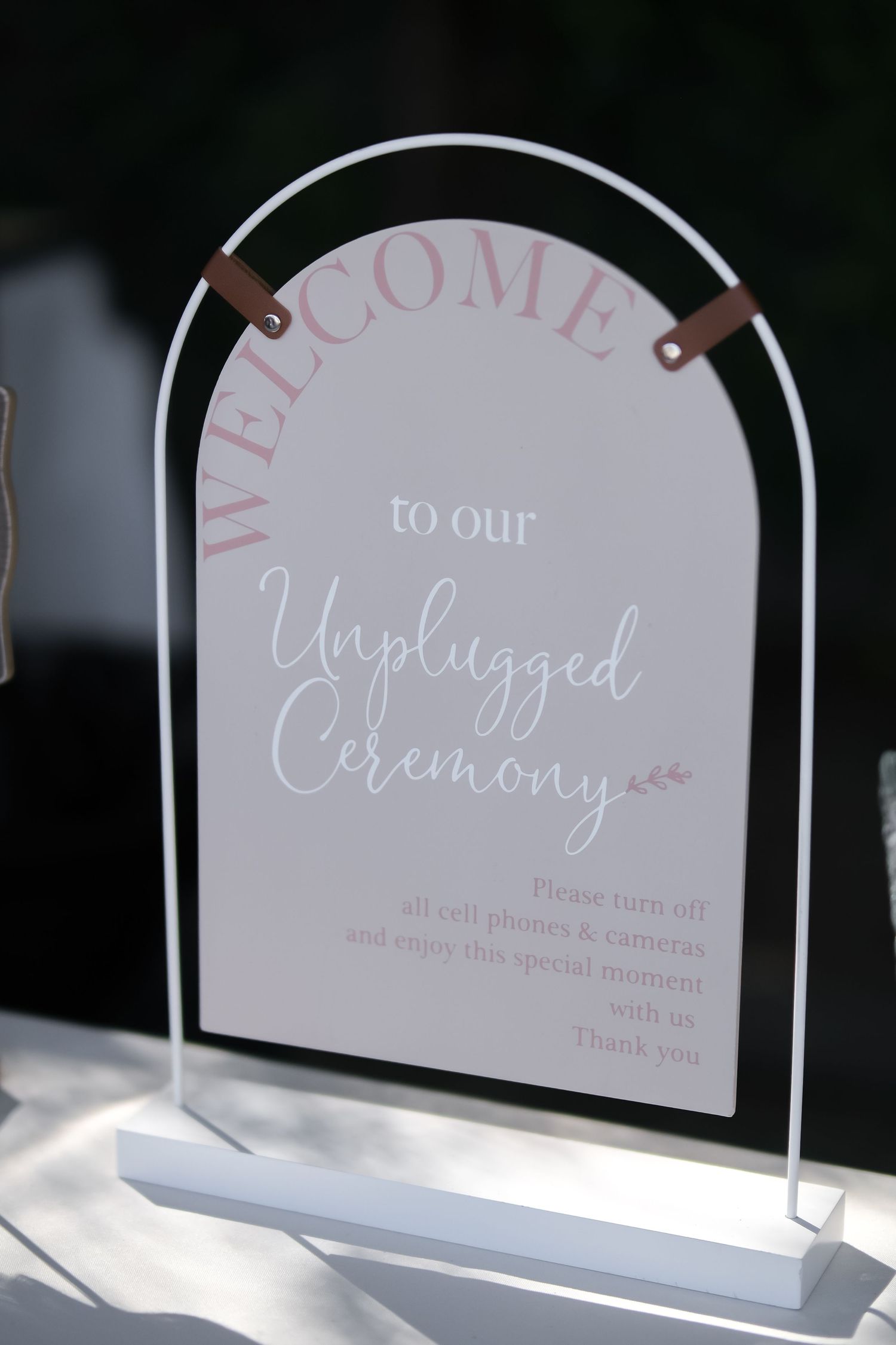 Elegant acrylic wedding sign welcoming guests to an unplugged ceremony, asking them to turn off phones and cameras.