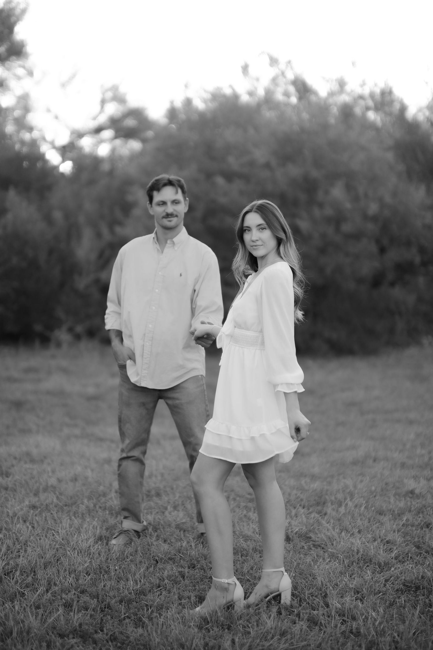 Black and white portrait of couple standing in field during engagement session.