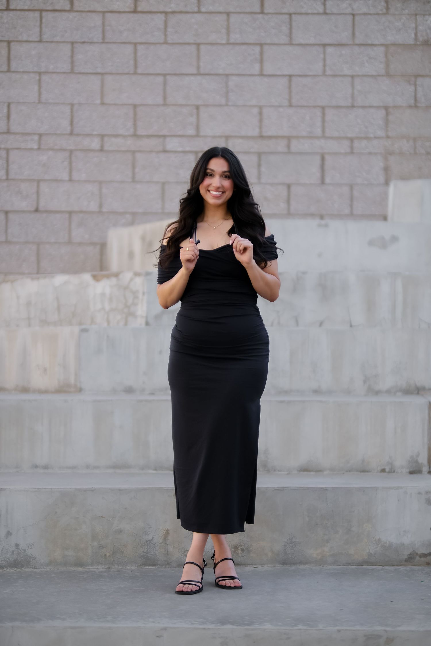A person in a black dress poses in four different stances against a stone wall background.