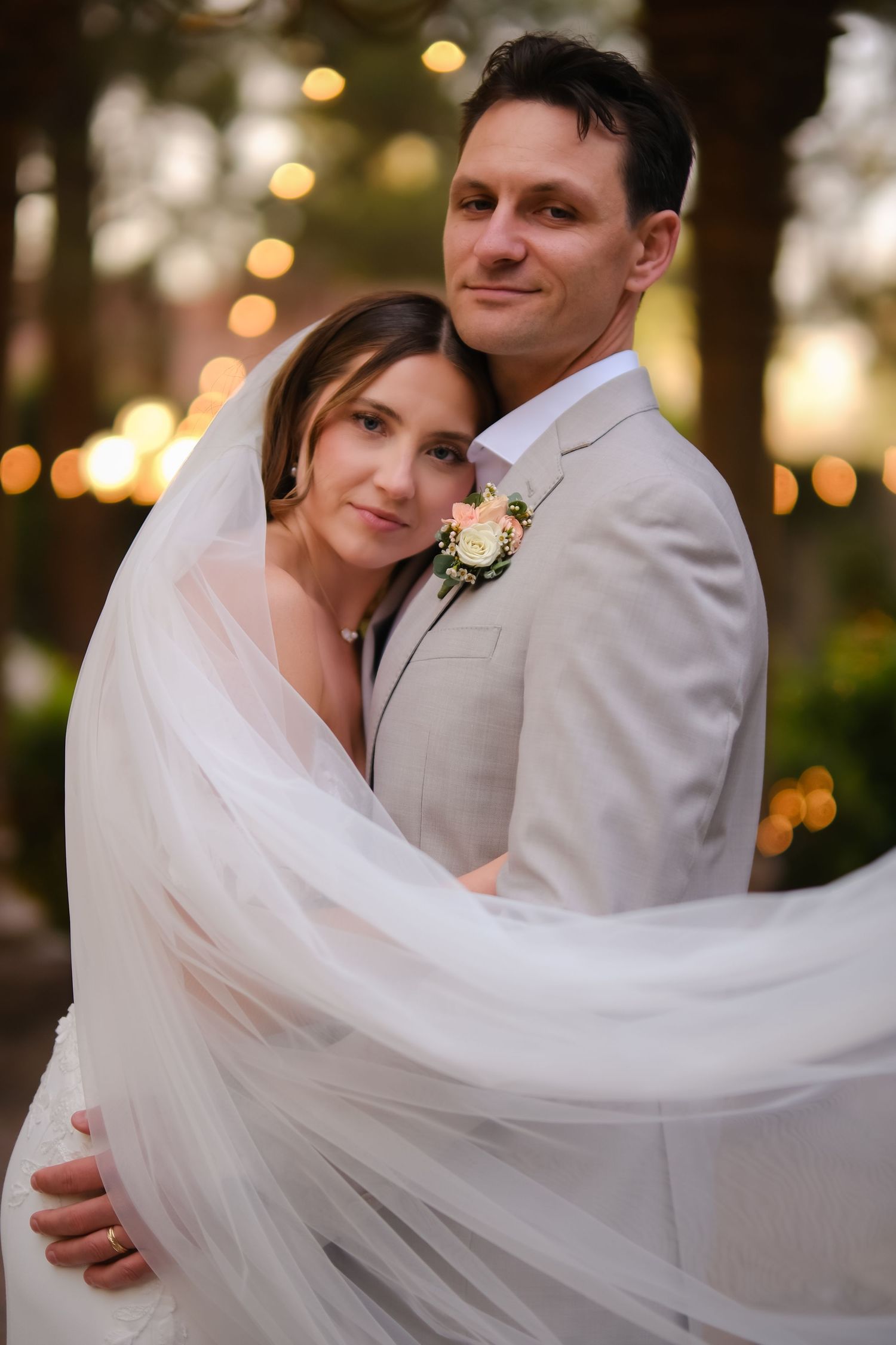 A romantic wedding portrait with flowing veil and soft bokeh lights in the background.